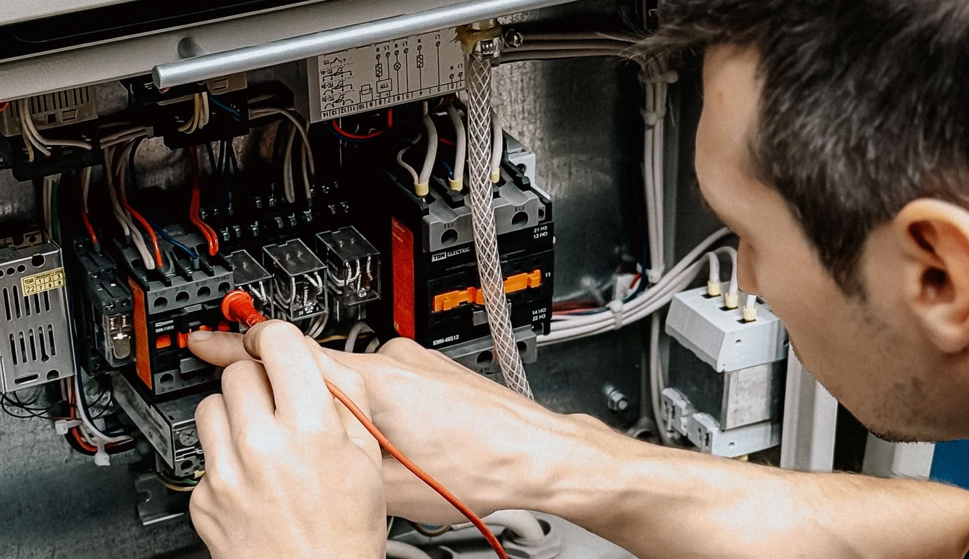 Électricien contrôlant au multimètre le câblage d’une armoire électrique.
